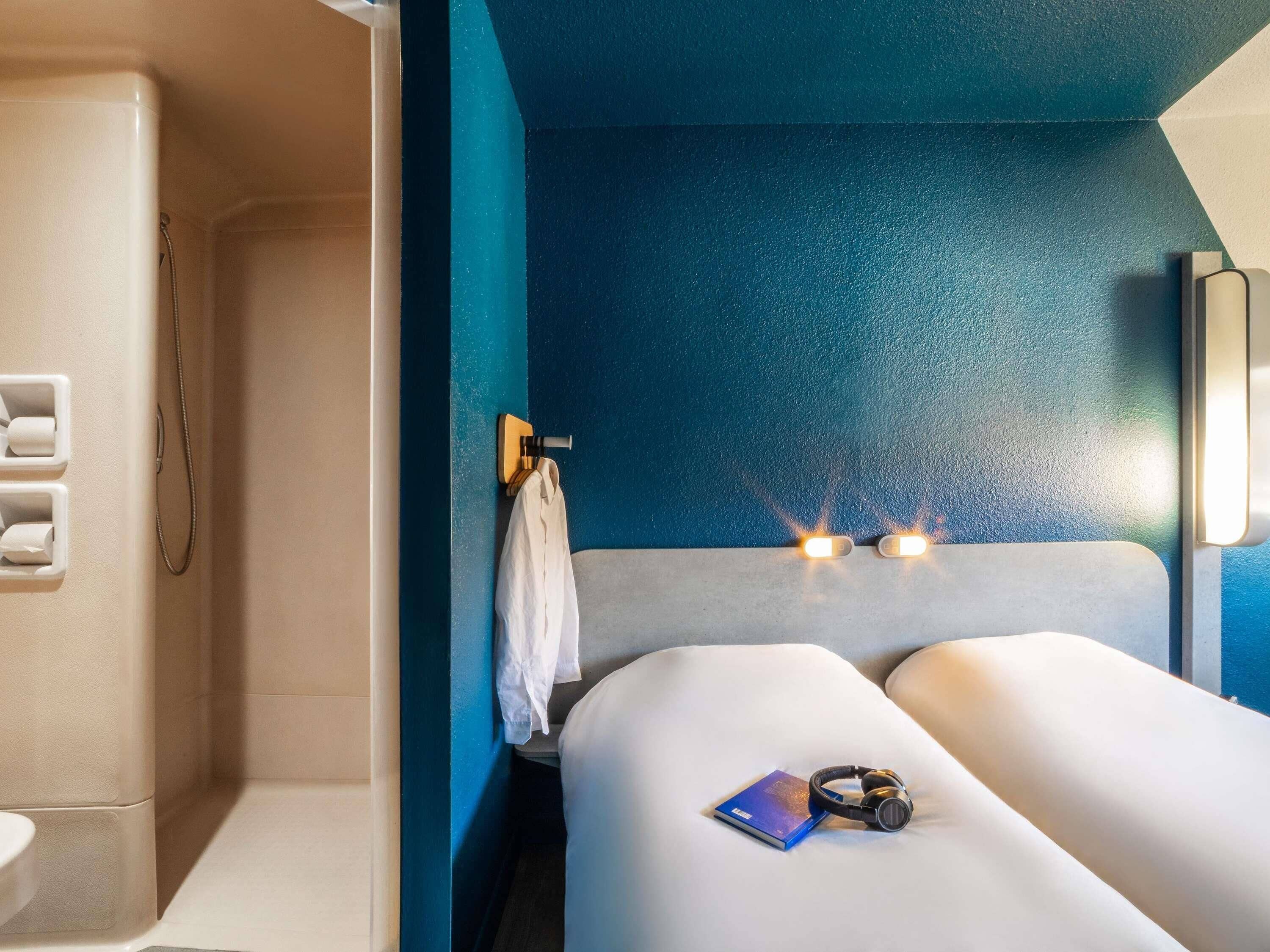 Een moderne hotelkamer met een douche, een bed met kussen, een boek en headphones.
