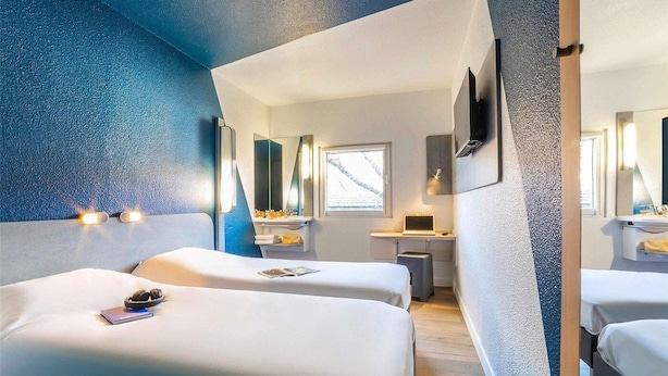 Een hotelkamer met twee bedden, een bureau, een spiegel en een raam.