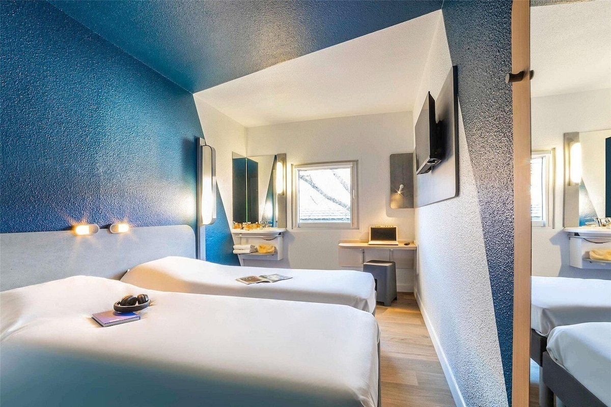 Een hotelkamer met twee bedden, een bureau, een spiegel en een raam.