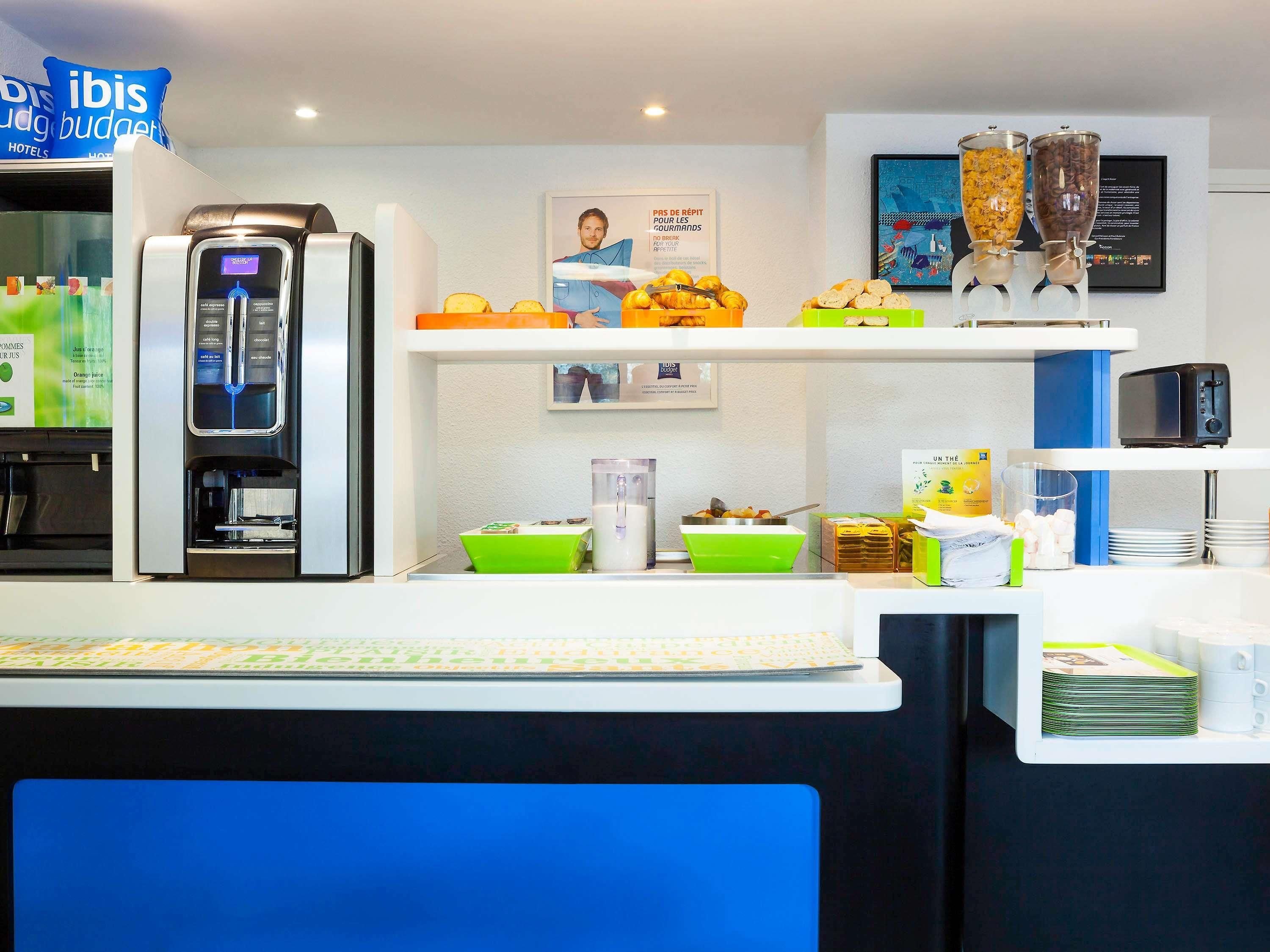 A hotel reception area with a coffee machine, breakfast options, and a framed picture on the wall.