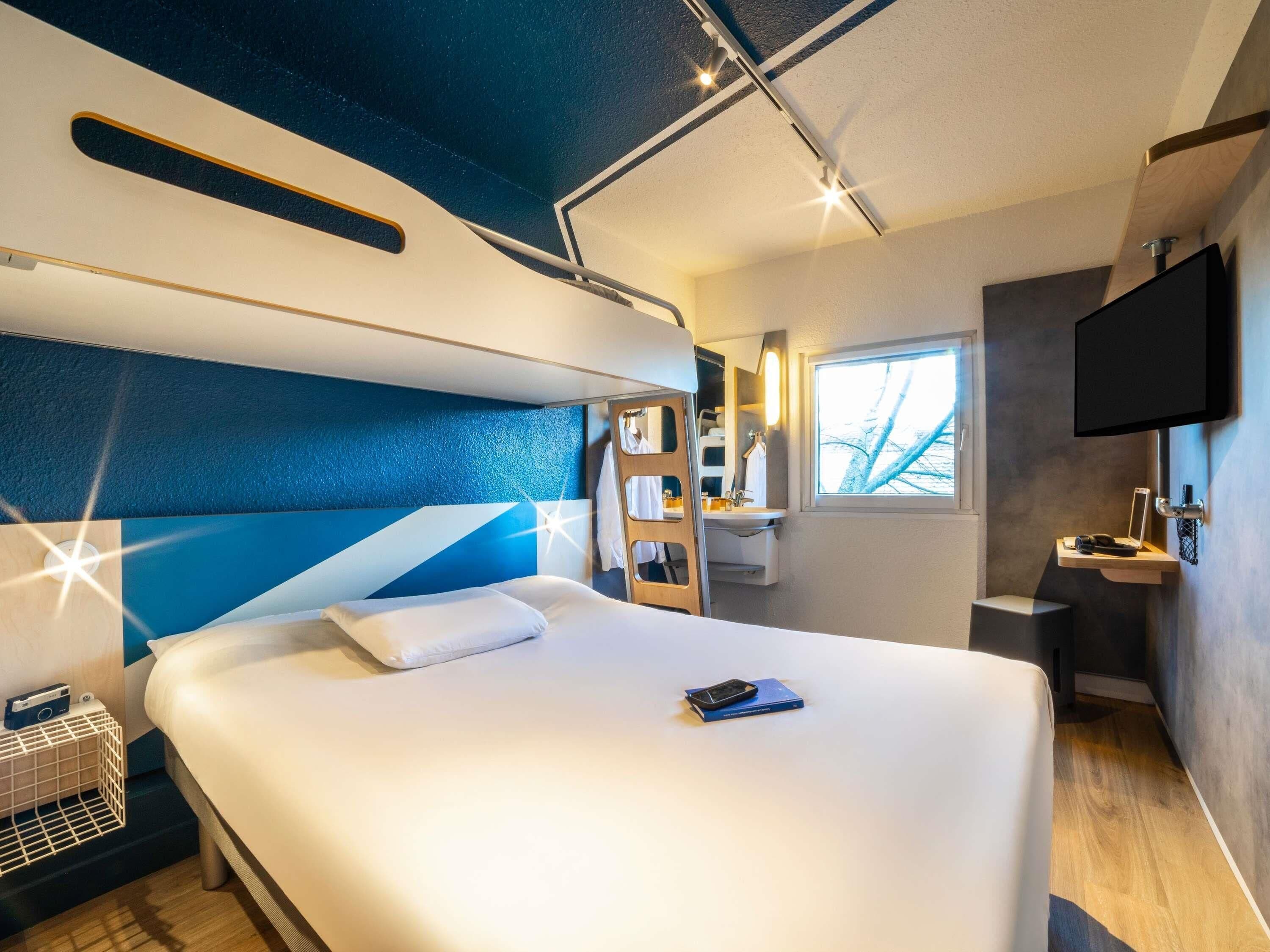 Een moderne hotelkamer met een groot bed, een kleine badkamer, een aan de muur bevestigde televisie en een raam dat natuurlijk licht binnenlaat.