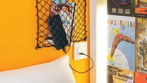 Een kamer met een bed, een wandcontactdoos, een wit kussen en een poster van een kangoeroe.