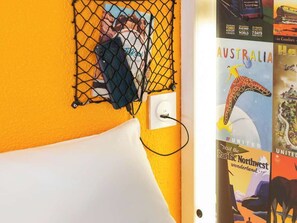 Een kamer met een bed, een wandcontactdoos, een wit kussen en een poster van een kangoeroe.