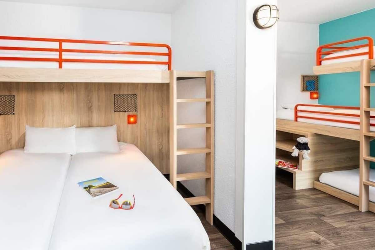 A room with bunk beds, a wooden ladder, a white bed, and a small shelf with a teddy bear.