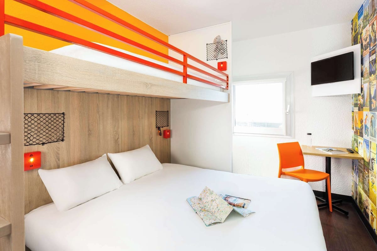 Une chambre avec un lit superposé, un bureau avec une chaise, une télévision et un mur orné d’une affiche colorée.