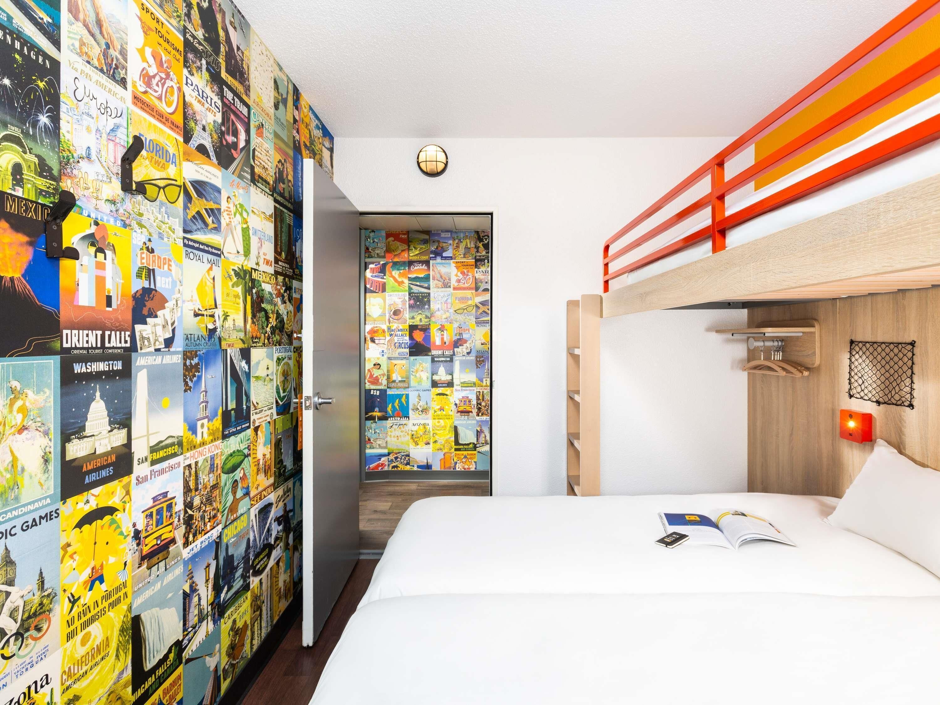 Une chambre avec un lit superposé, un mur décoré d’affiches de voyage, une porte ornée d’un globe terrestre et une petite table sur laquelle se trouvent un livre et un téléphone.