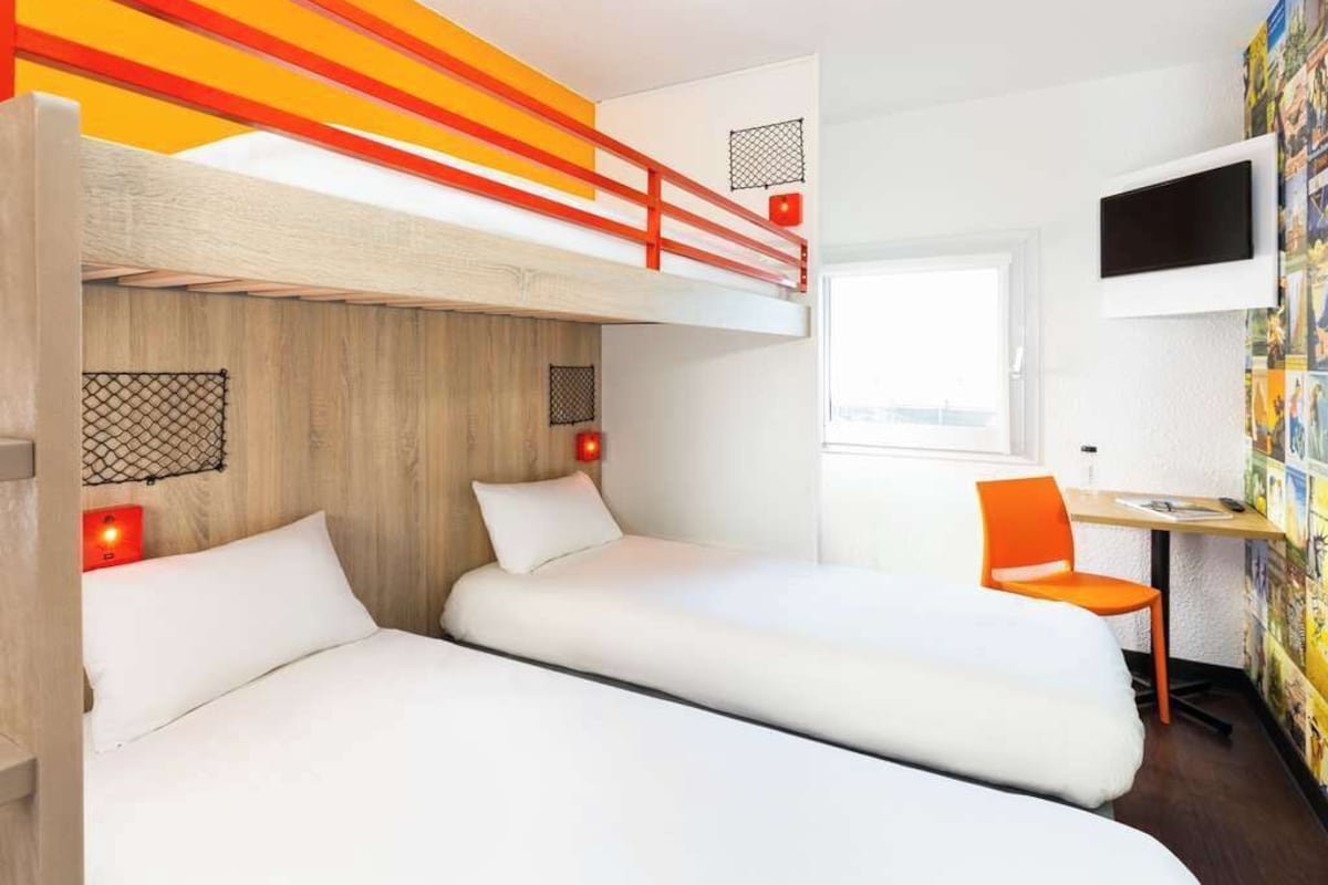 Een kamer met twee bedden, een bureau, een televisie en een raam.