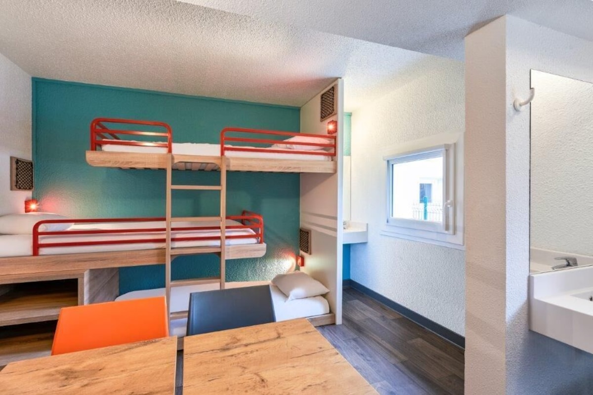 Een slaapkamer met een stapelbed, bureau, raam en badkamer.