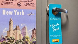 Een deur met een blauw hotelbord waarop 'On the Road' en 'NE PAS DÉRANGER DO NOT DISTURB' staat.