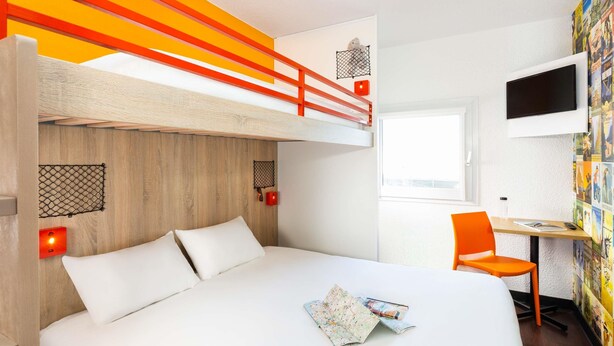 Een moderne hotelkamer met een stapelbed, een bureau met een stoel, een televisie en een muur met een poster.