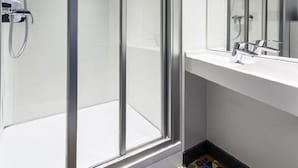 Een moderne badkamer met een douchecabine van glas, een grote spiegel en een witte wastafel.