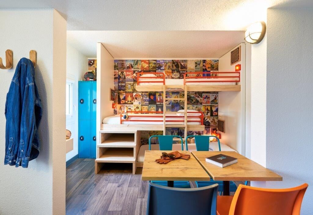 Habitación con literas, una pared llena de carteles, un escritorio con una silla y un armario azul.