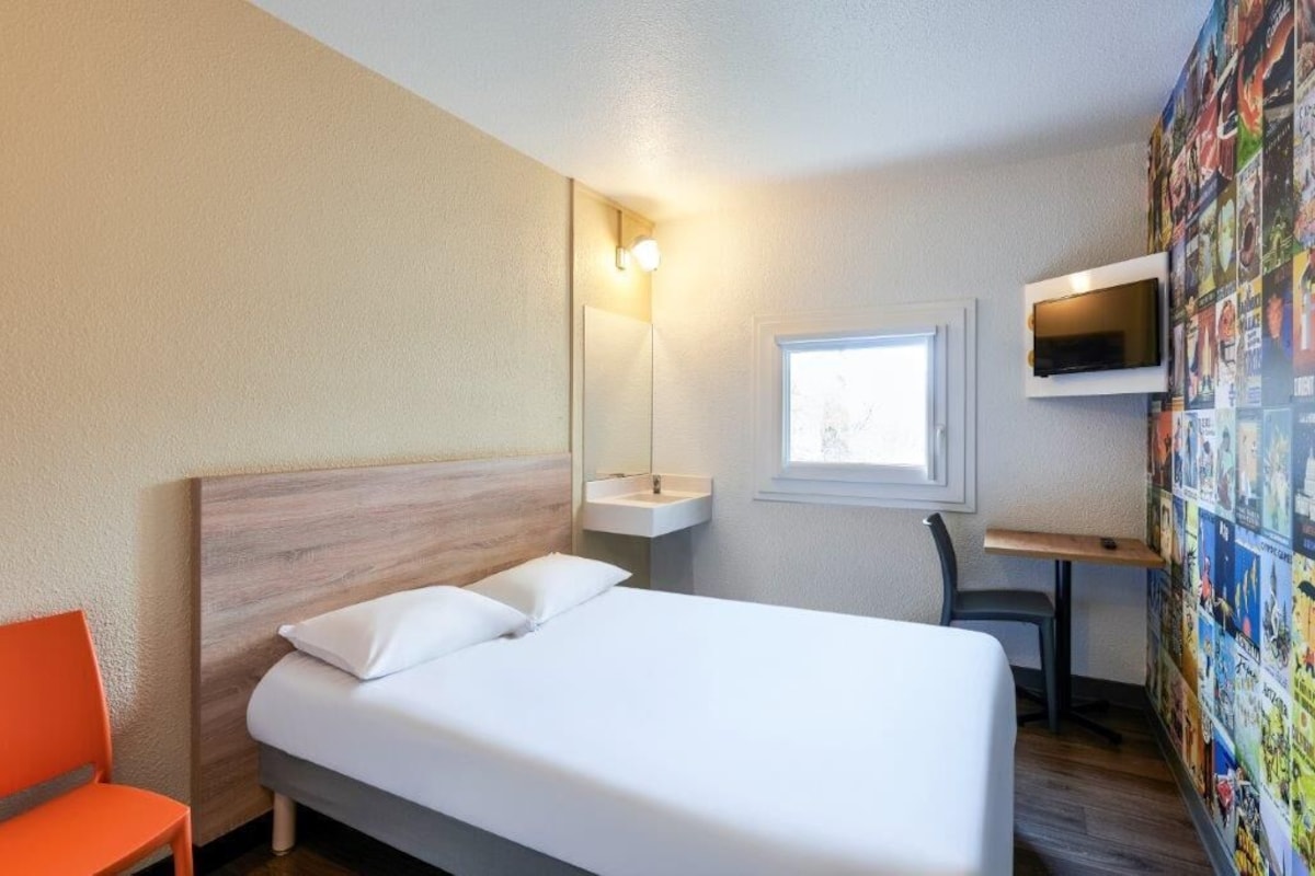 Een hotelkamer met een bed, bureau, stoel, televisie, raam en een muur met een poster.