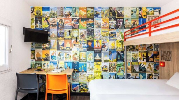 Une chambre avec un lit superposé, un bureau, une chaise et un mur recouvert d’affiches de voyage.