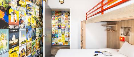 A room with a bunk bed, a wall decorated with travel posters, a door with a globe, and a small table with a book and a phone.