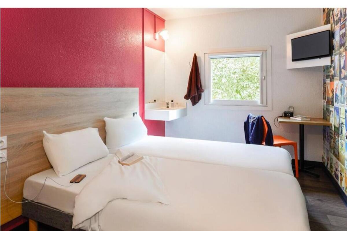 Une chambre d’hôtel avec un lit, un petit bureau, une télévision et une fenêtre donnant sur un paysage verdoyant.