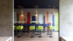 A modern interior with a bar area, high stools, and a wall with vertical color accents. - ibis budget Tarbes (Tarbes)