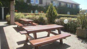 An outdoor seating area with picnic tables, a building in the background, and well-maintained landscaping. - ibis budget Tarbes (Tarbes)