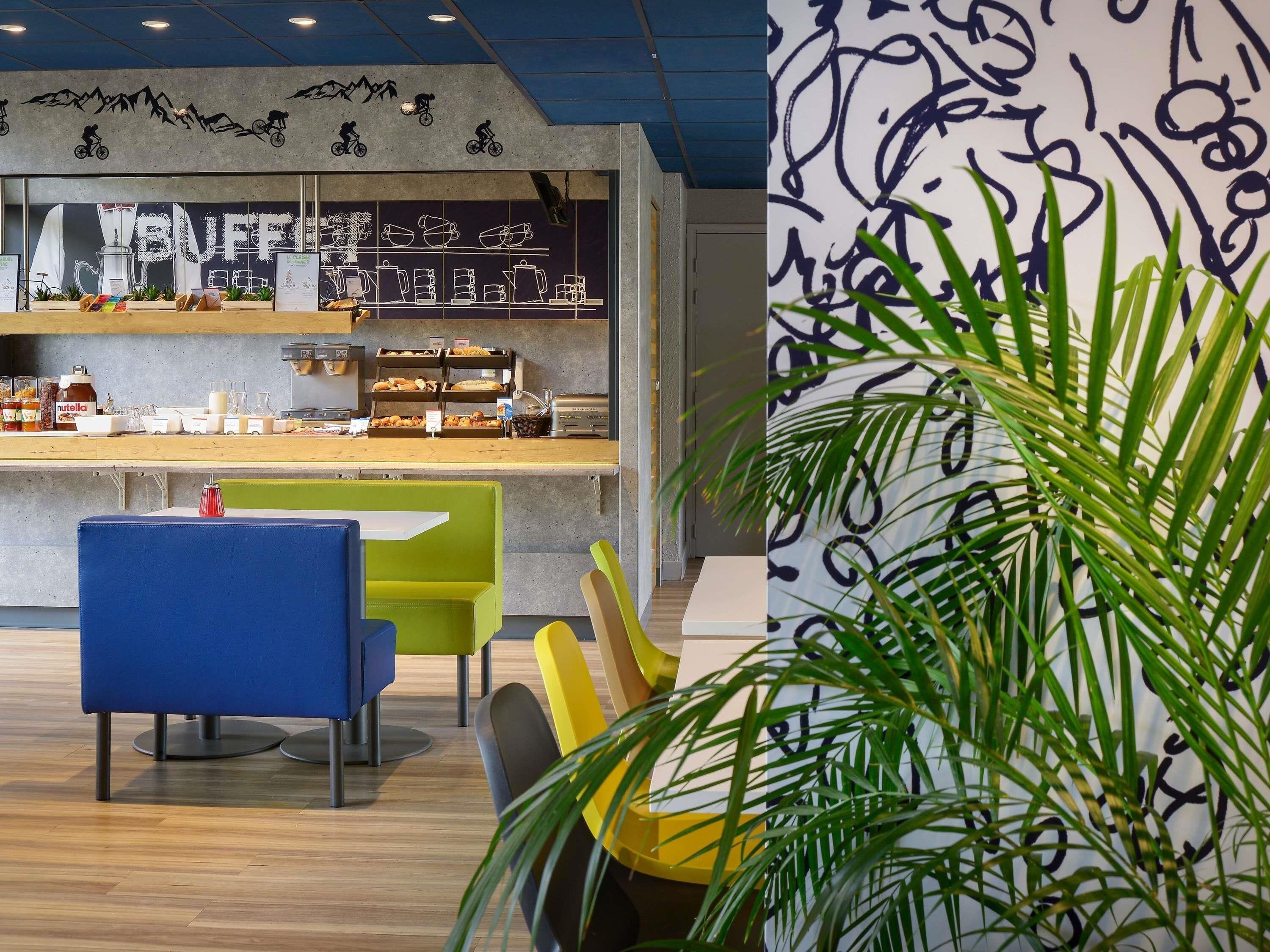 A modern cafe interior with a counter displaying coffee and pastries, seating with colorful chairs, and decorative wall art.