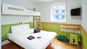 A hotel room with a bunk bed, a bedside table with a lamp, a TV mounted on the wall, and a window with a view of buildings. - ibis budget Toulouse Centre Gare (Toulouse)