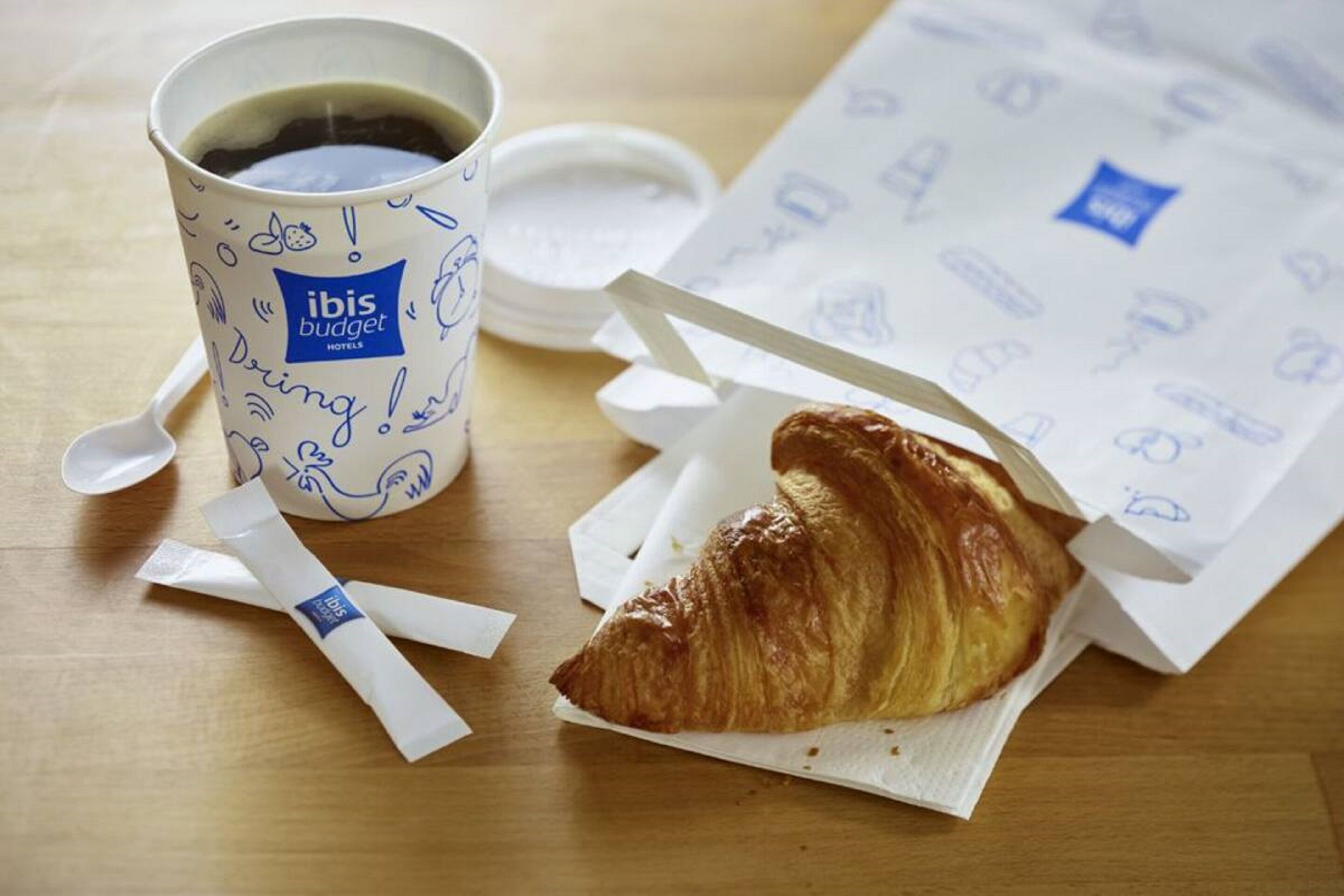 A cup of coffee, a croissant, and a napkin on a wooden table.