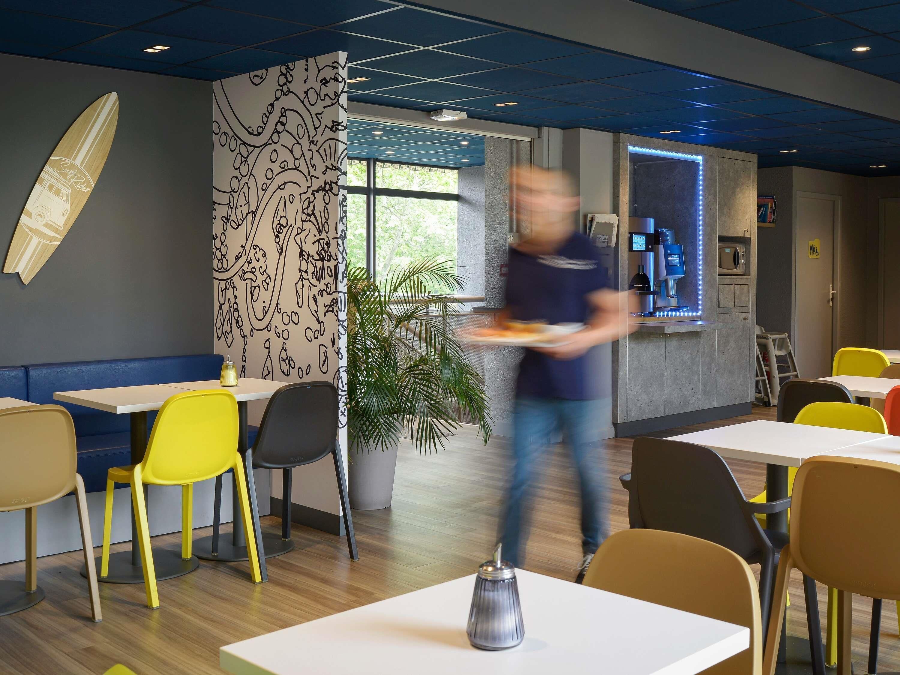 Un restaurant moderne avec un intérieur caractérisé par un plafond bleu, une décoration sur le thème du surf et un bar éclairé d’une lumière bleue.