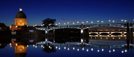 Vista nocturna de un puente con luces iluminadas que se reflejan en el agua.