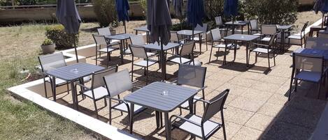 An outdoor patio with multiple tables and chairs, some with umbrellas.