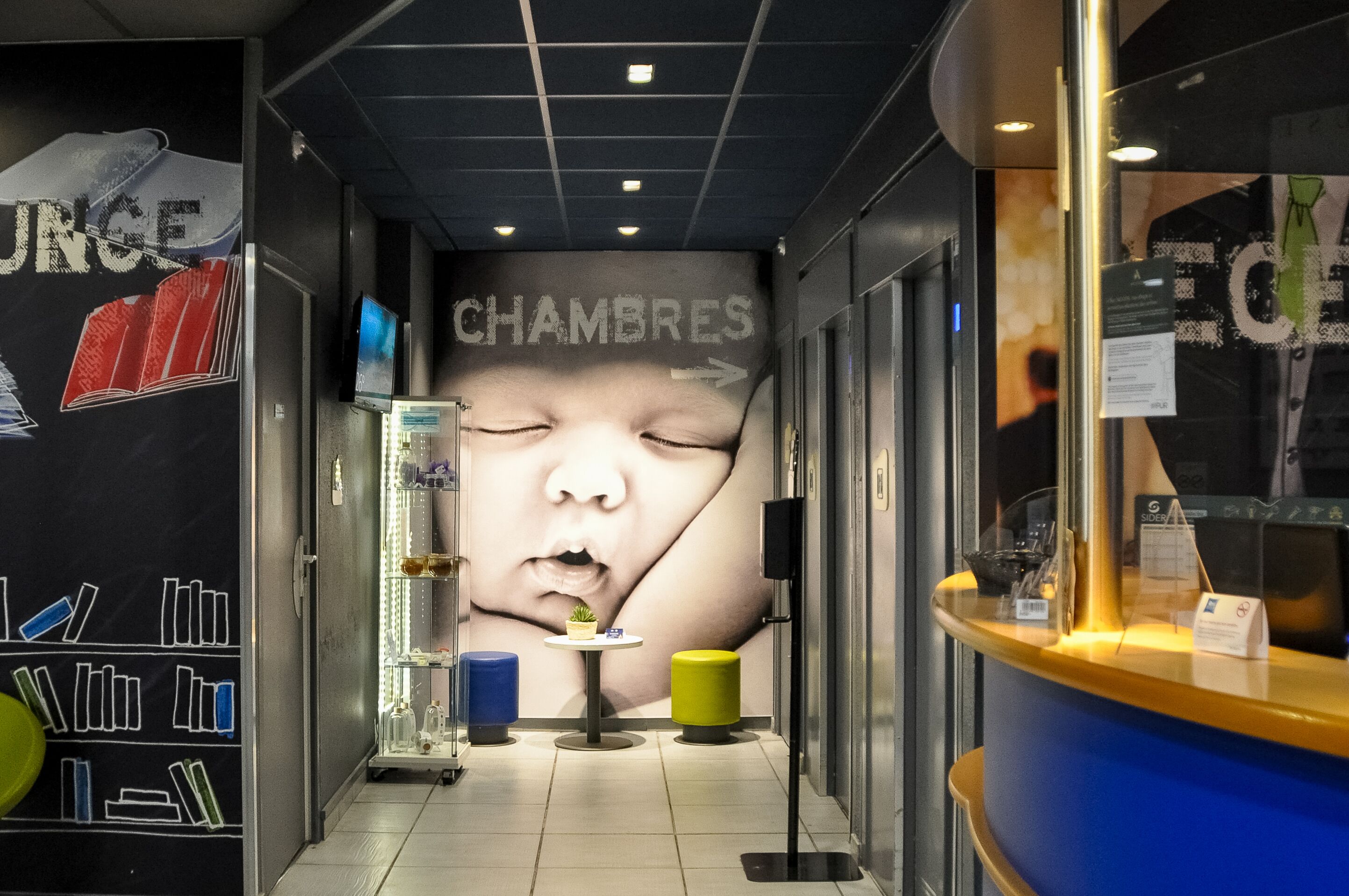 A corridor with a wall mural, a reception desk, and a small seating area with a table and chairs.