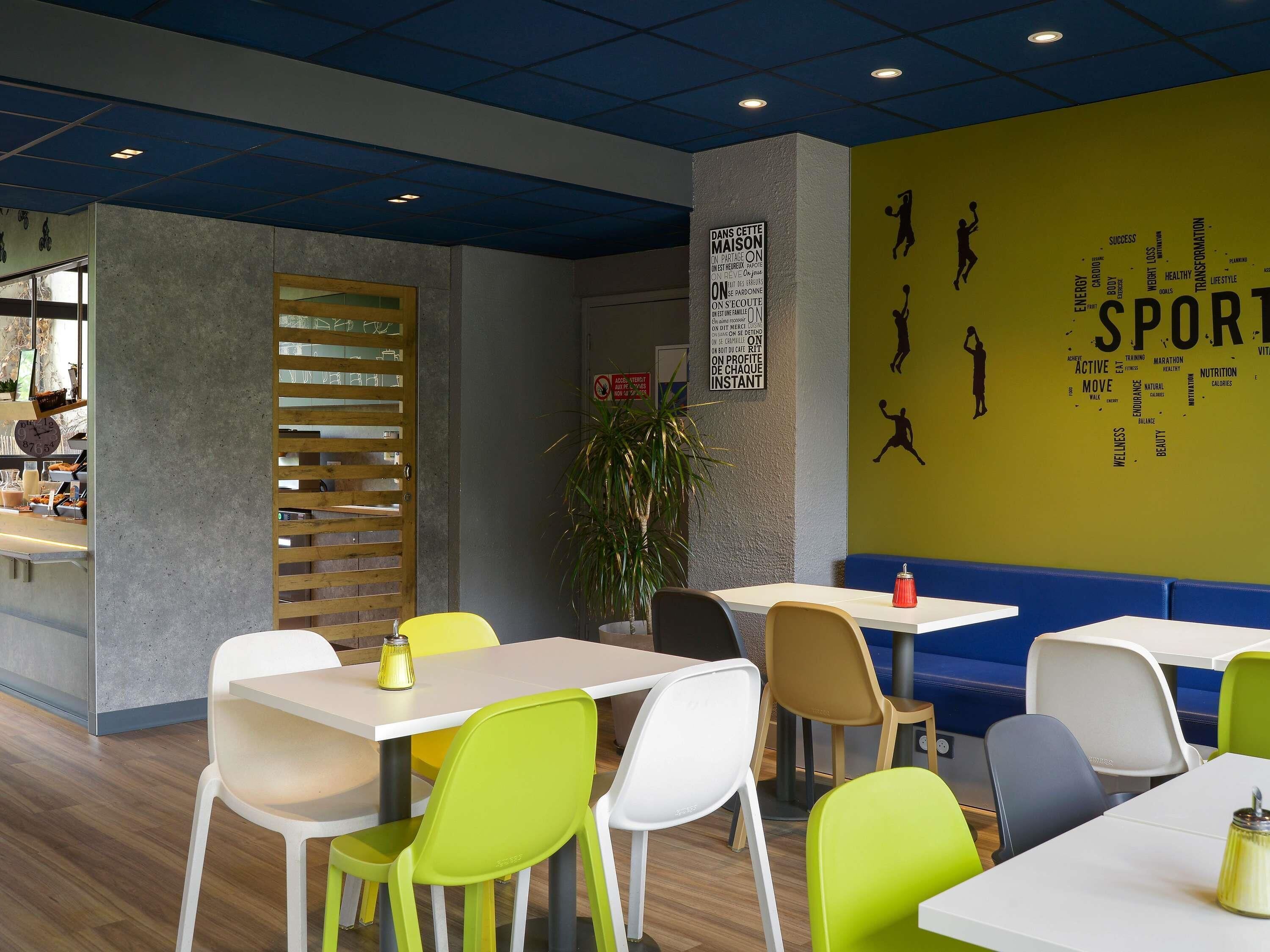 Un espace intérieur moderne, doté de tables et de chaises, d’un mur orné de mots liés au sport et d’un panneau affichant un texte motivant.