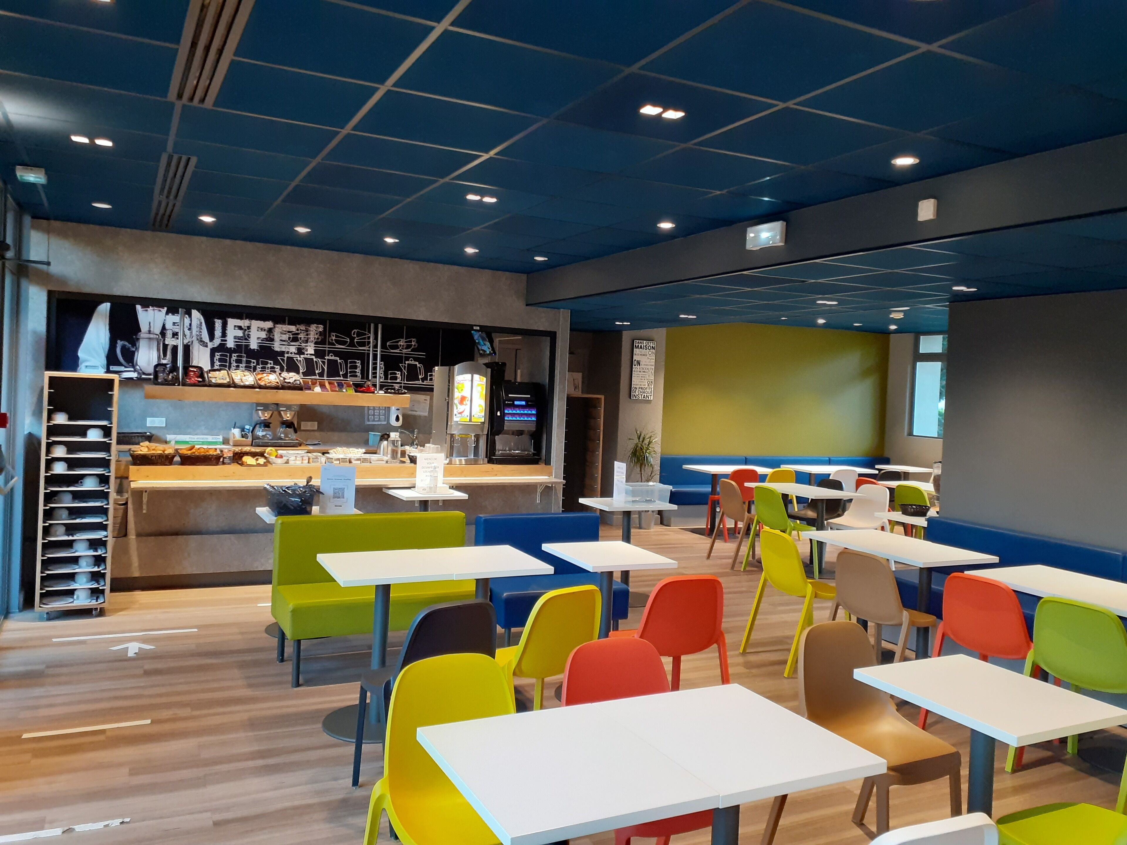 A modern cafe with colorful chairs and tables, a counter with food items, and a menu board.