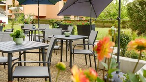 Outdoor patio furniture with umbrellas, a potted plant, and a view of a residential building. - ibis budget Toulouse Centre Gare (Toulouse)