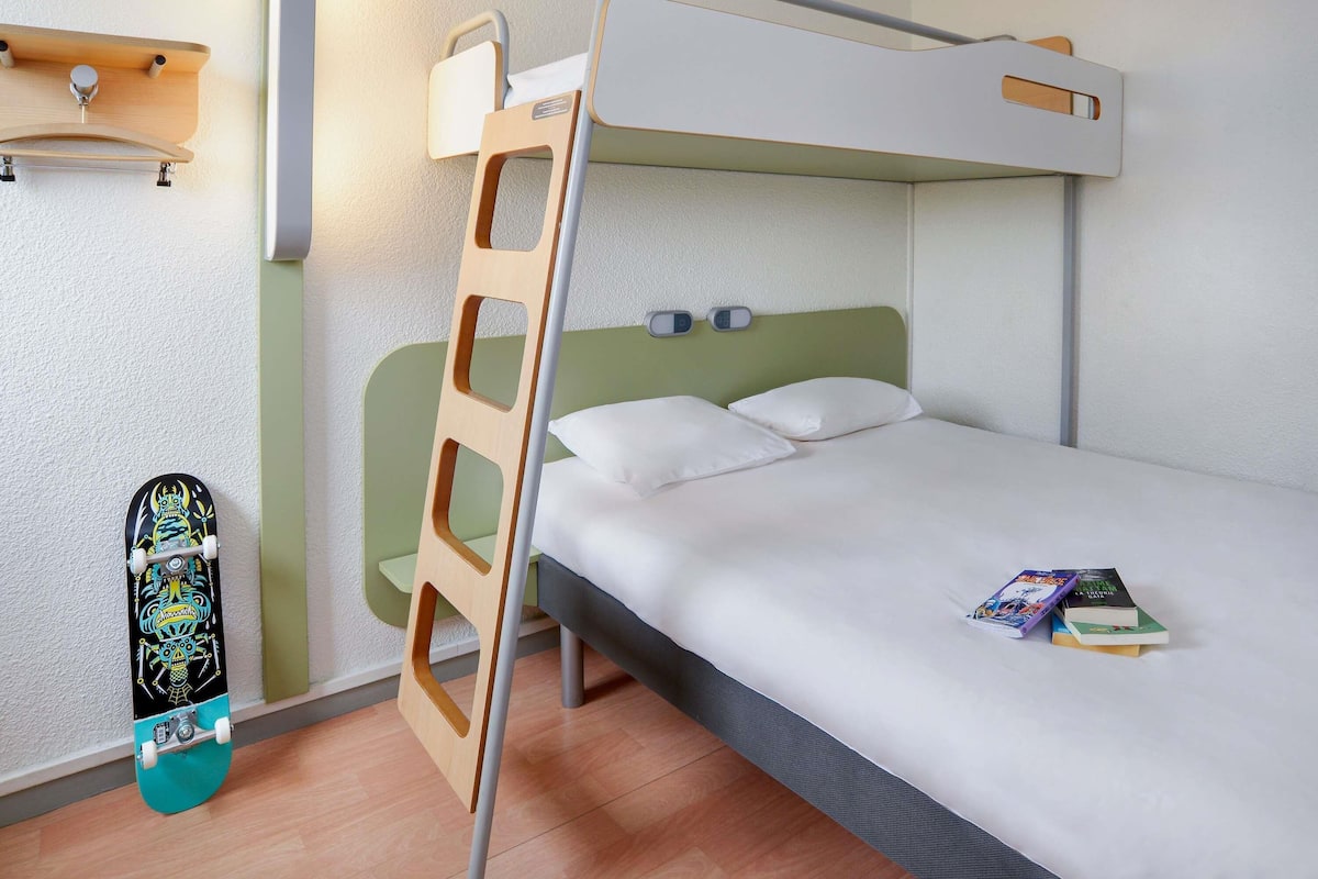 Ein Stockbett mit einer Leiter, ein Nachttisch, ein Wandregal und ein Skateboard.