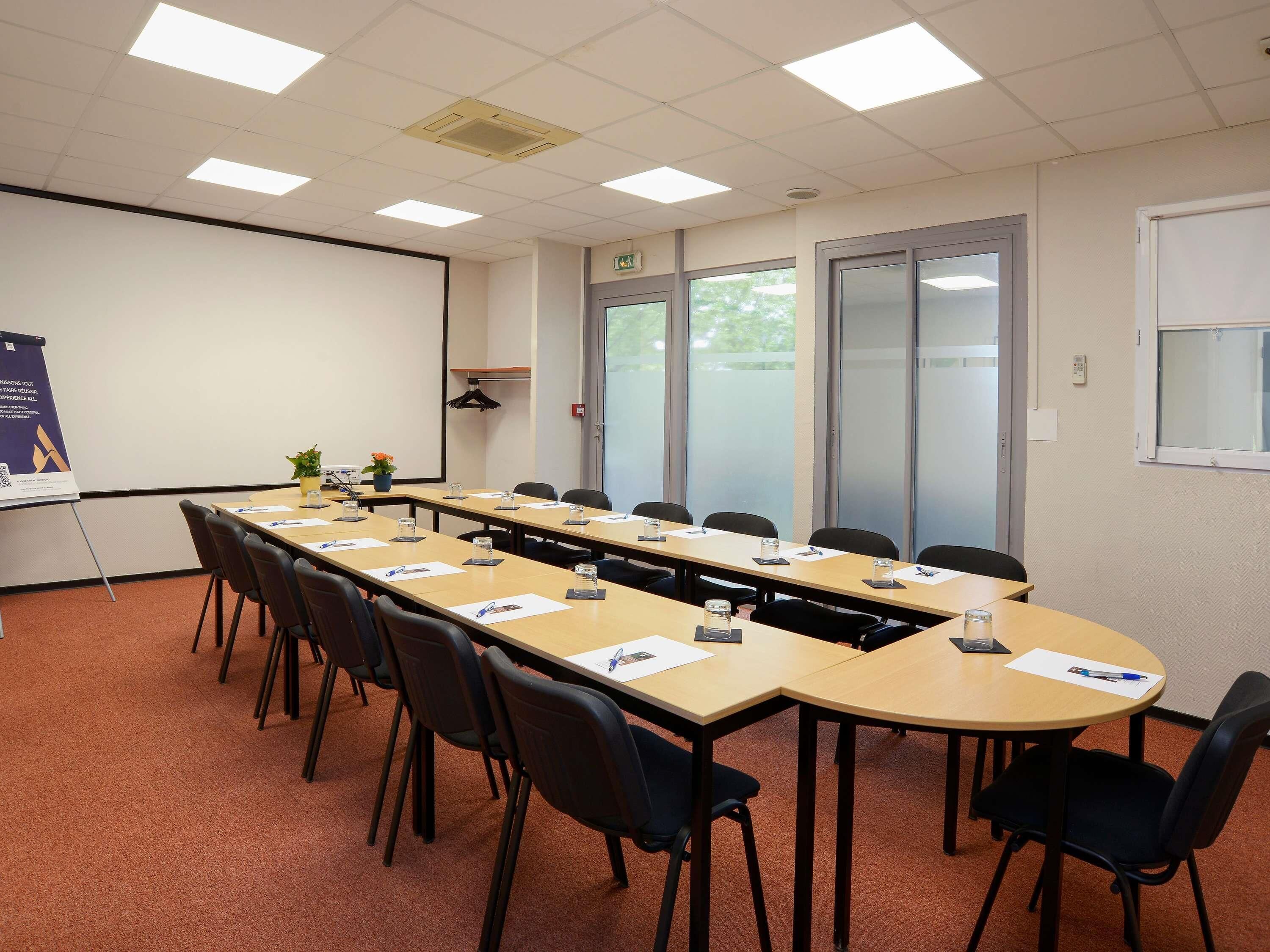 A conference room with a long table, chairs, a projector screen, and a whiteboard.