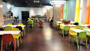 A cafeteria with multiple tables and chairs, a counter with a coffee machine, and a refrigerator in the background. - ibis budget Paris Porte de Bercy (Charenton-le-Pont)