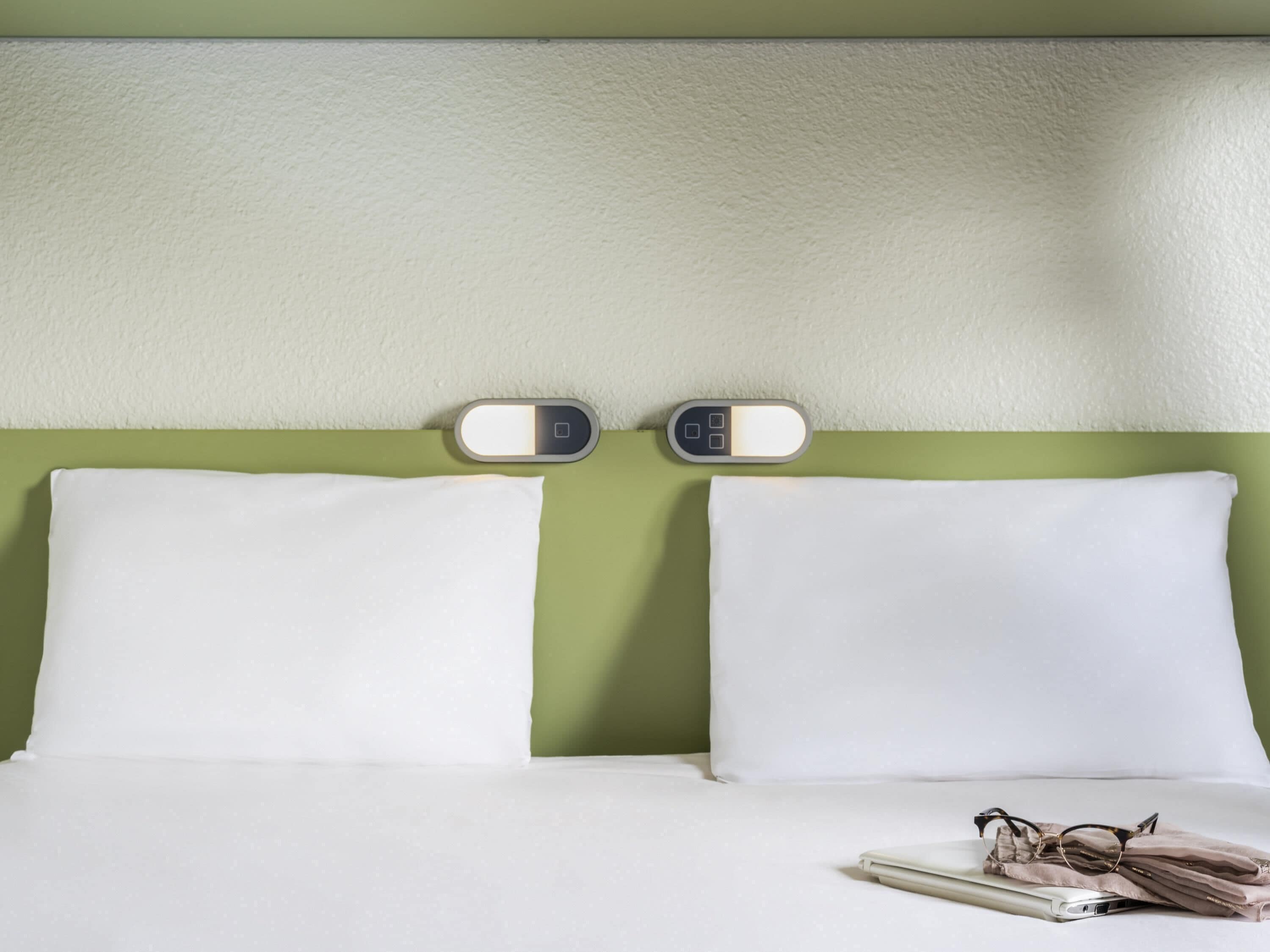 A bed with white pillows and a digital clock on the headboard.