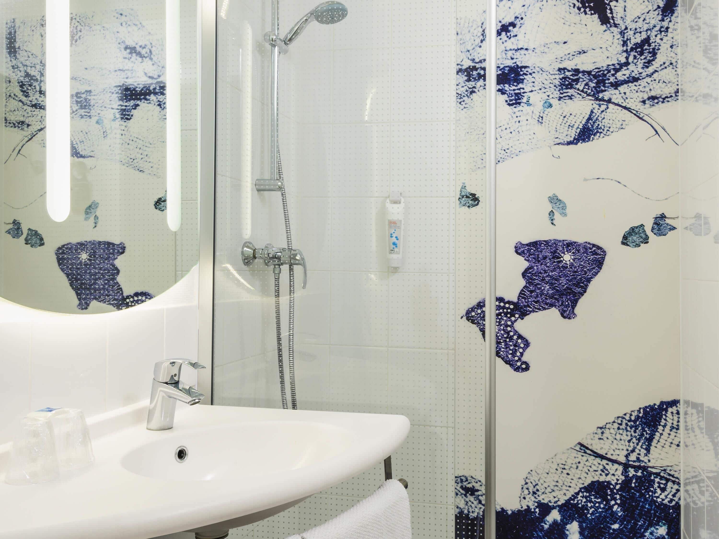 Une salle de bain avec une douche à parois de verre, un lavabo blanc et des carreaux de mosaïque bleue décoratifs.