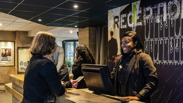 A reception desk with a modern design, featuring a wooden counter and a digital screen. - ibis budget Paris Porte de Bercy (Charenton-le-Pont)