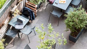Un patio al aire libre con mesas y sillas, rodeado de plantas y una valla de madera.