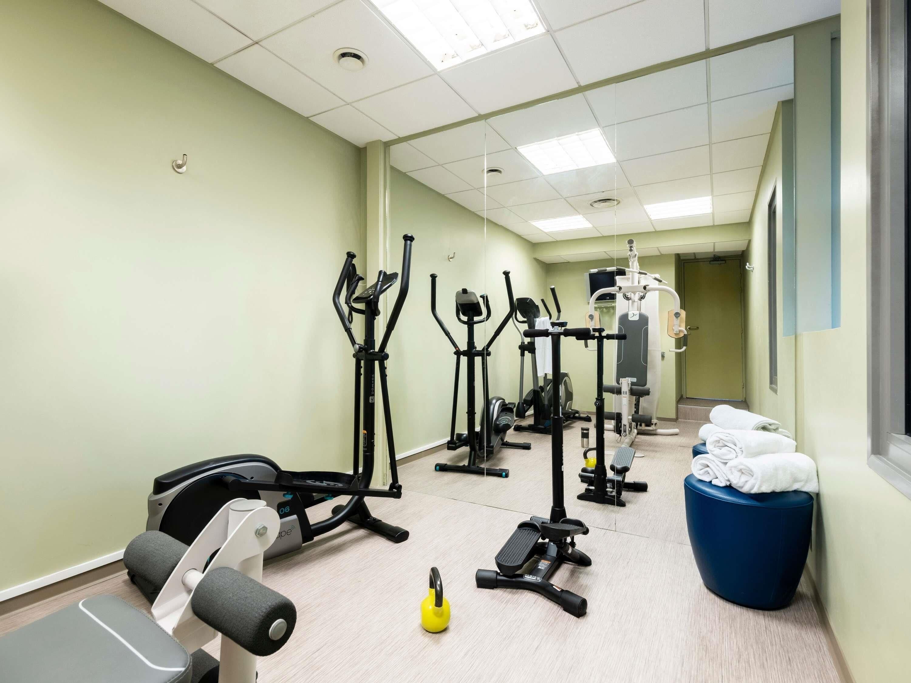 Un gimnasio con diferentes máquinas de ejercicio, un banco y un taburete azul.