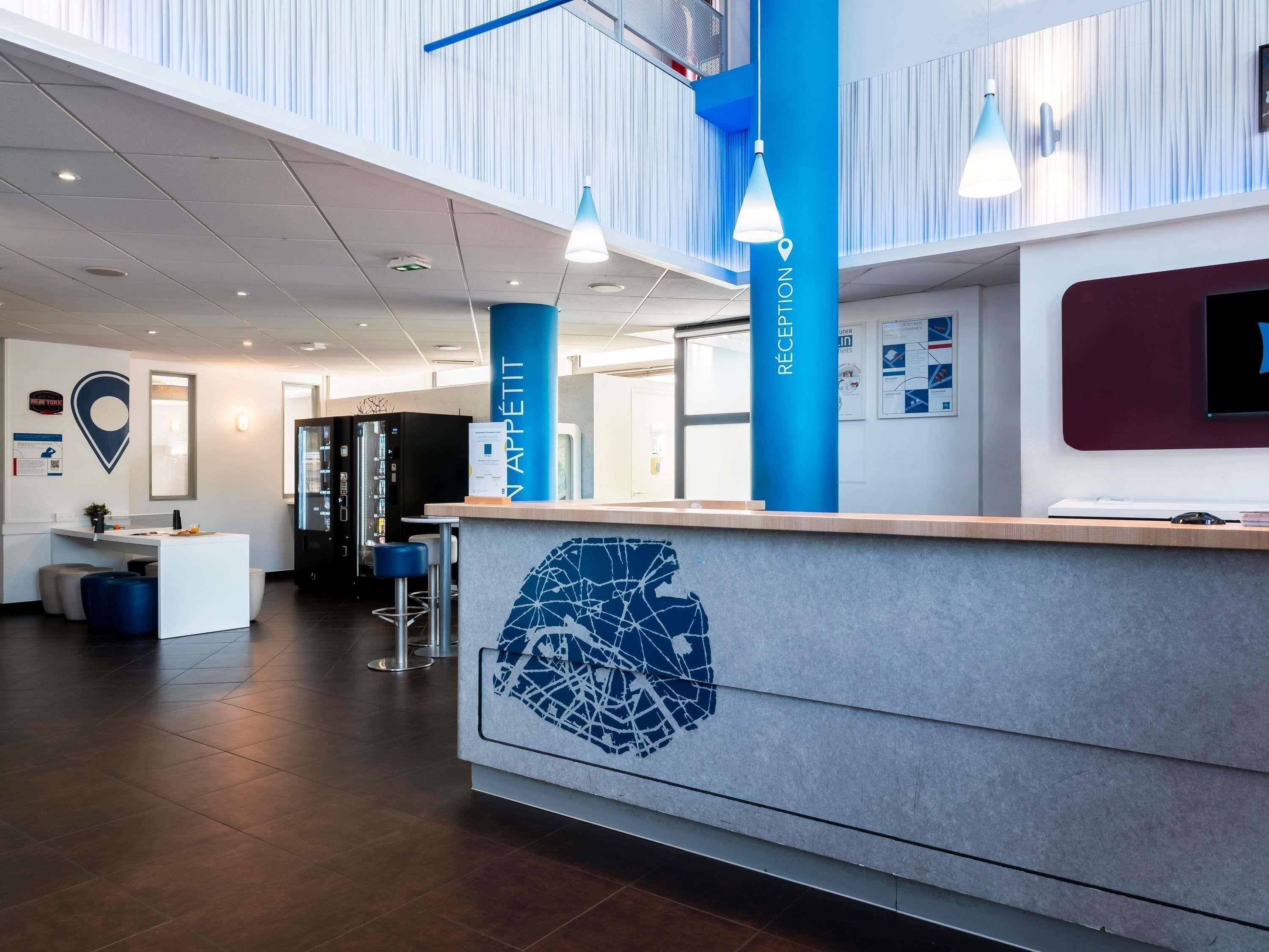 A reception desk with a map design, a blue pillar labeled 'RECEPTION,' and a modern interior with a high ceiling and bar stools.