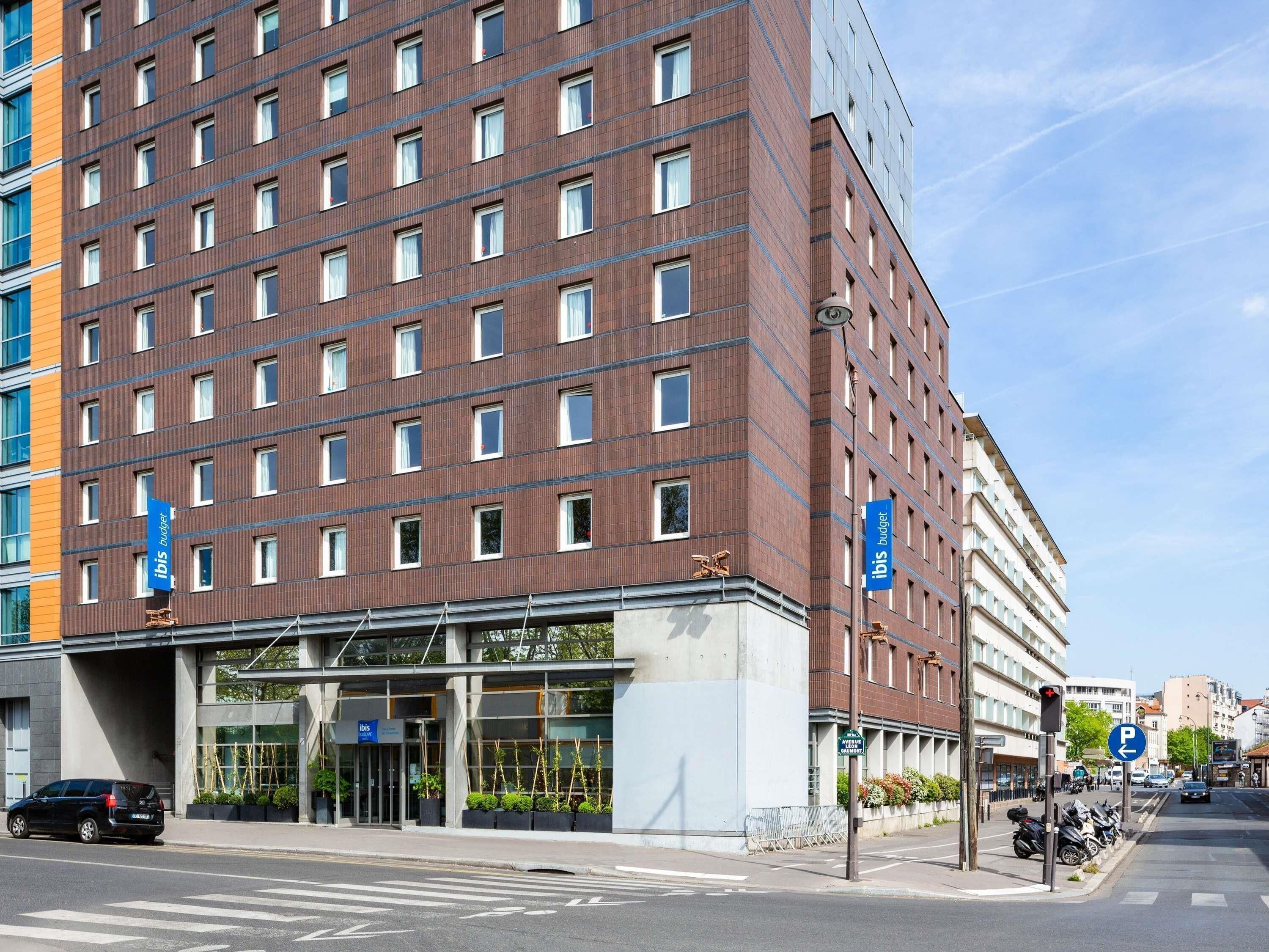 Un hotel de varios pisos con fachada de ladrillo moderno, entrada de vidrio y un letrero azul que dice 'ibis budget'.