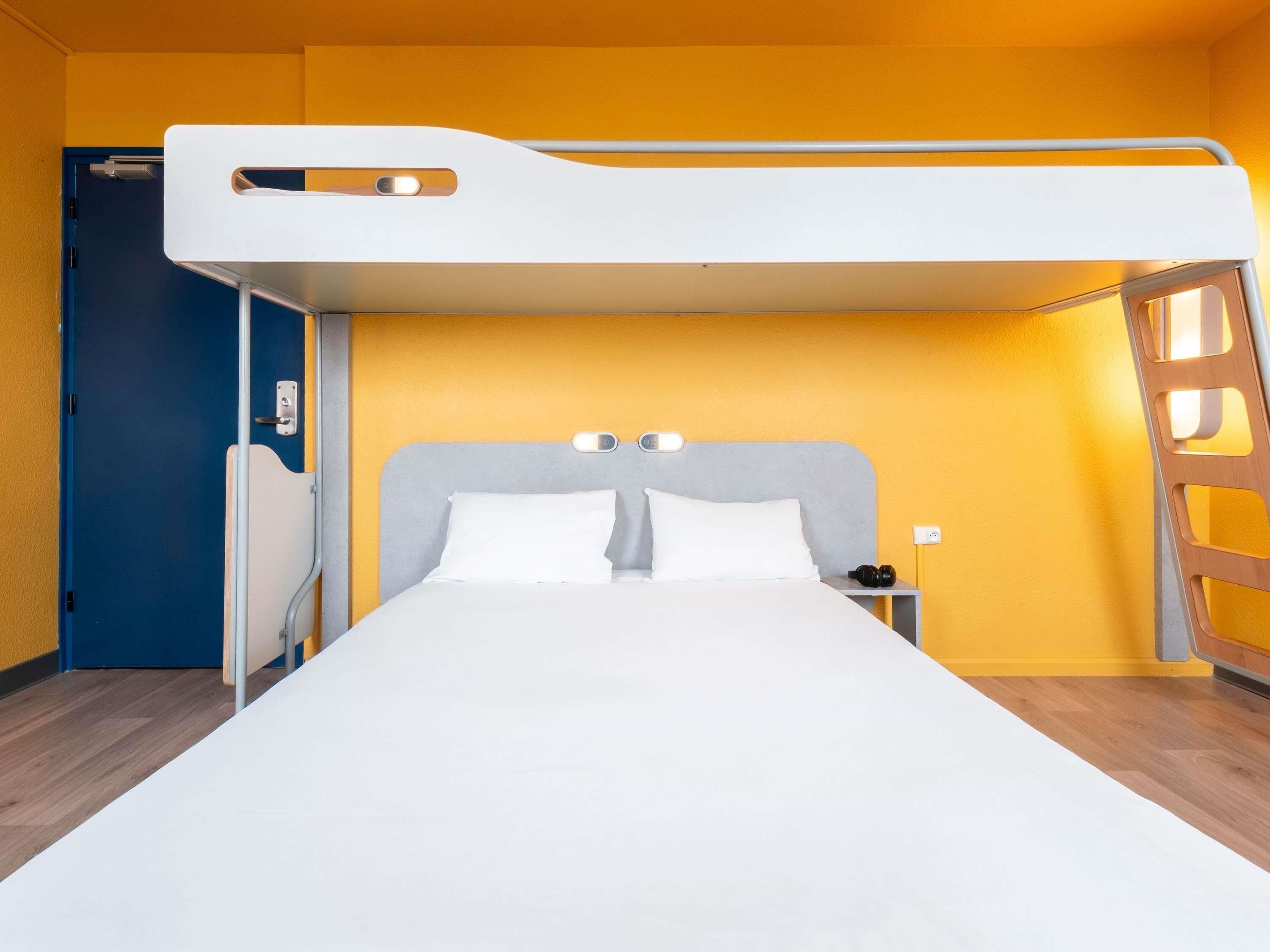 A bunk bed room with a blue door, a bedside table with a lamp, and a nightstand with a phone.