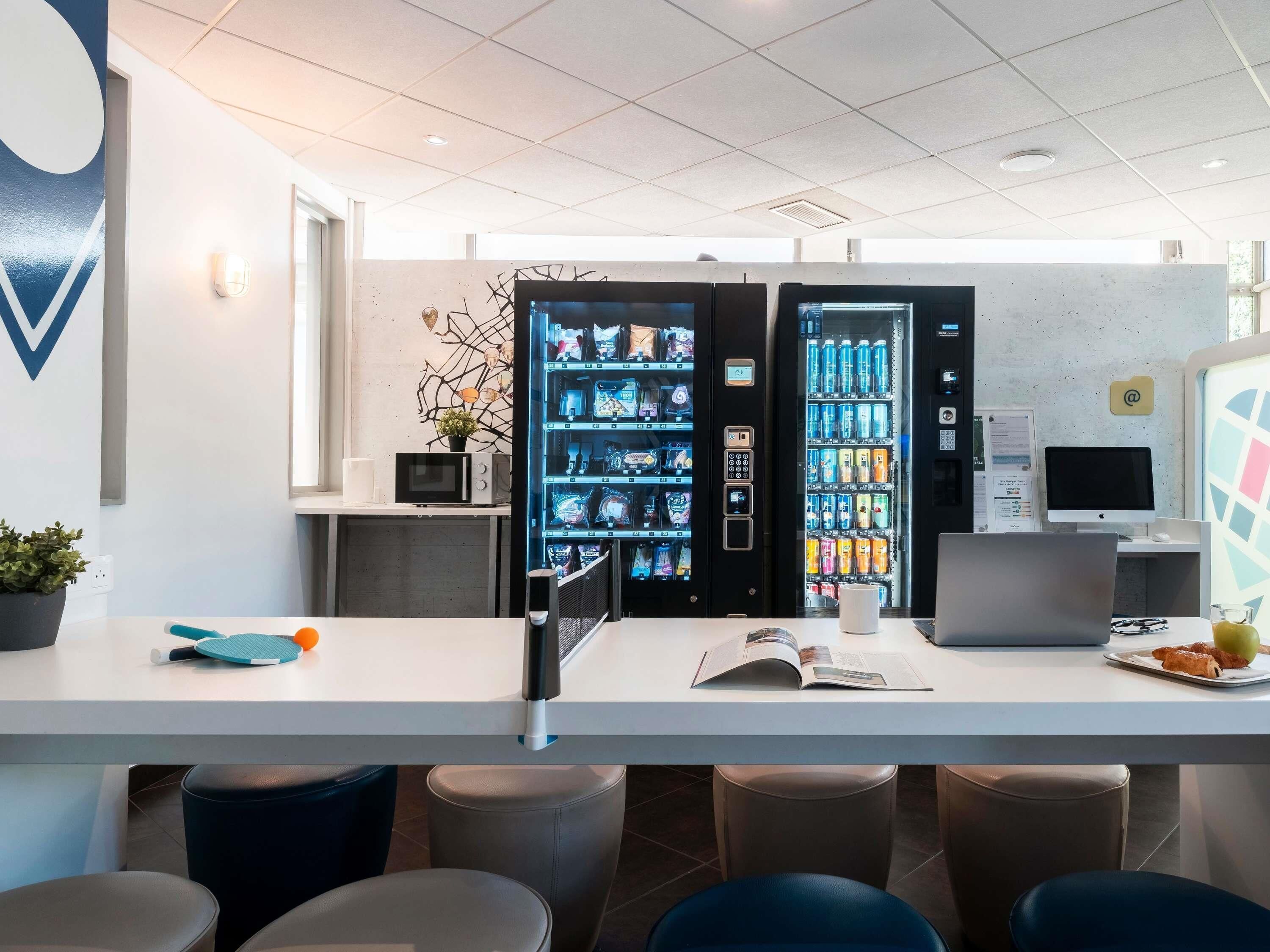 A modern office space with a white desk, vending machines, a computer, and a monitor.