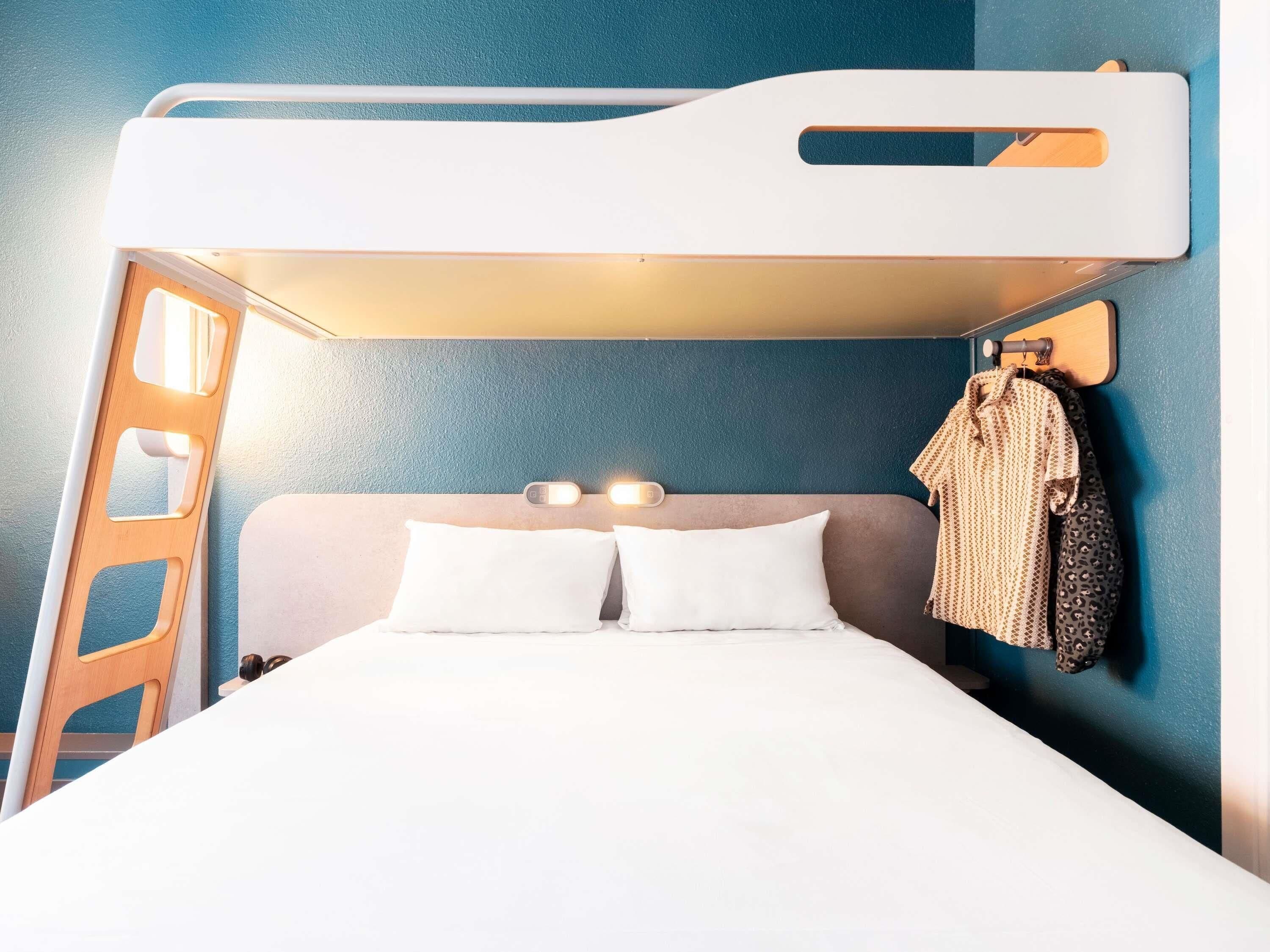 A bunk bed with a headboard, two pillows, a wall-mounted light, and a coat rack with a coat.