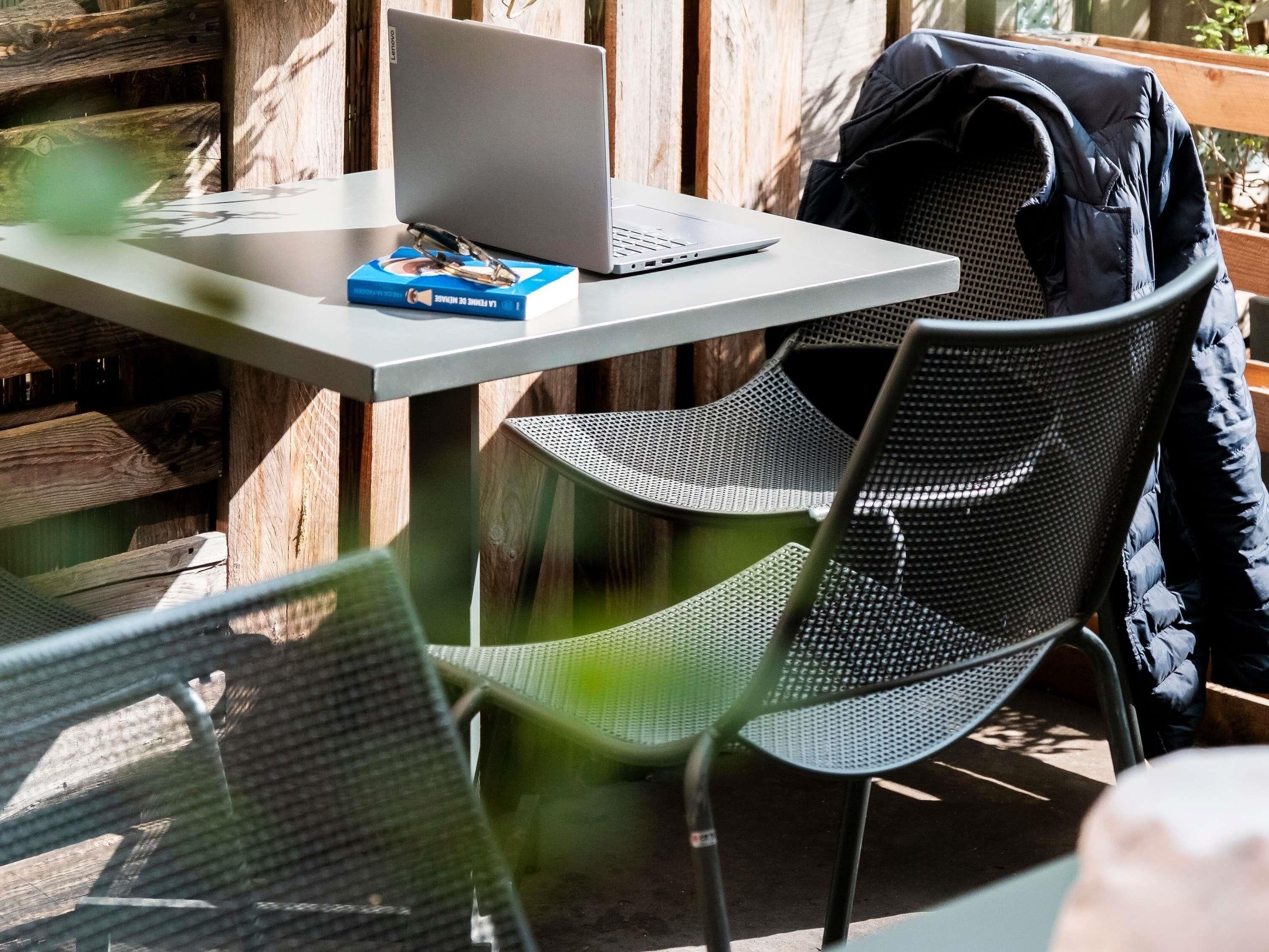 A table with a laptop, a book, and a pair of glasses. There are two chairs with mesh backs.