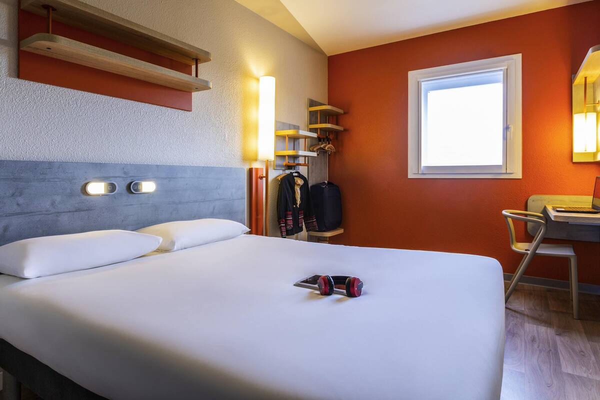 Une chambre d’hôtel avec un lit, un bureau et une chaise, une valise et une armoire.