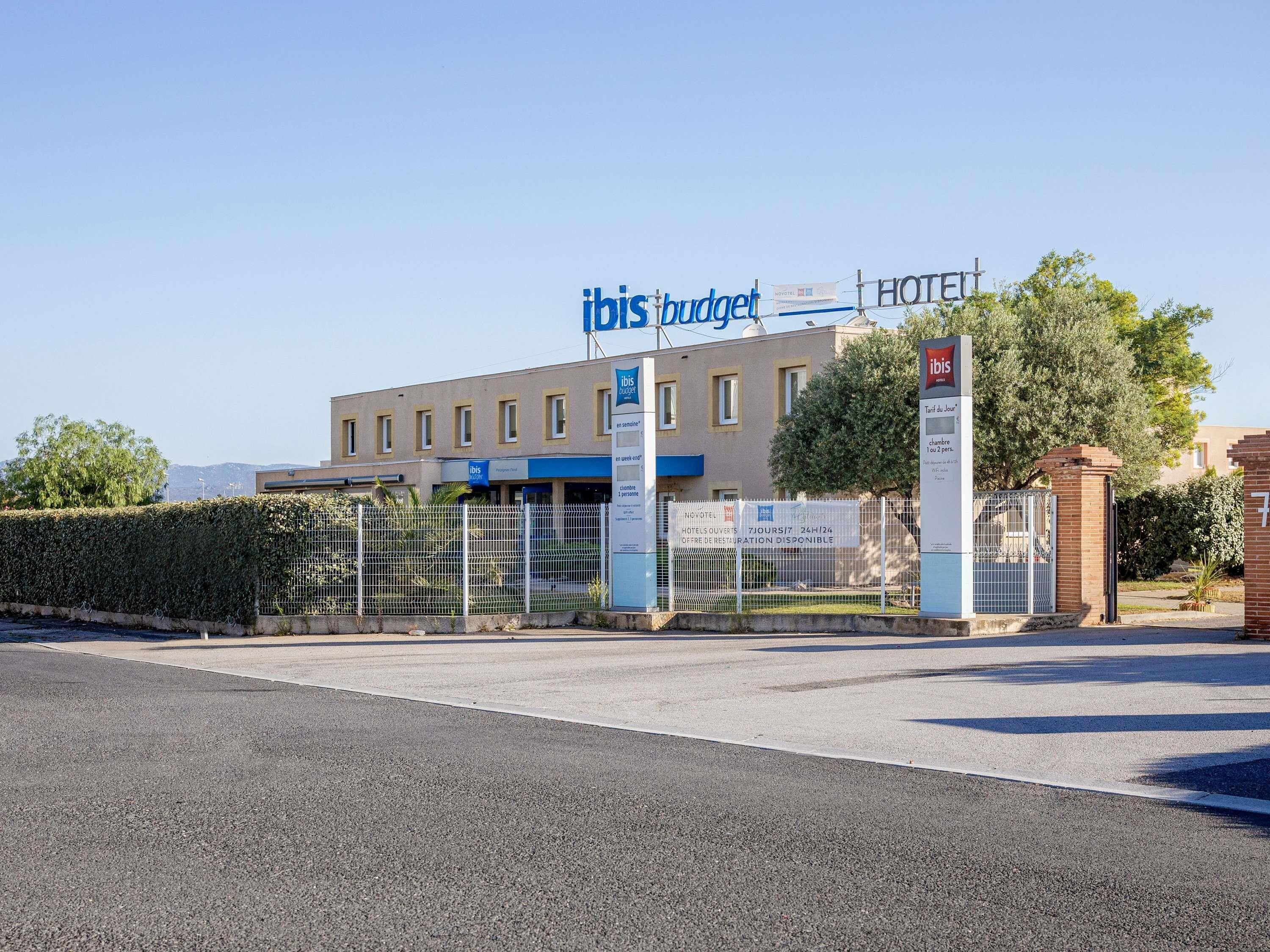 A hotel named ibis budget with a gated entrance, a sign indicating availability, and a clear sky.