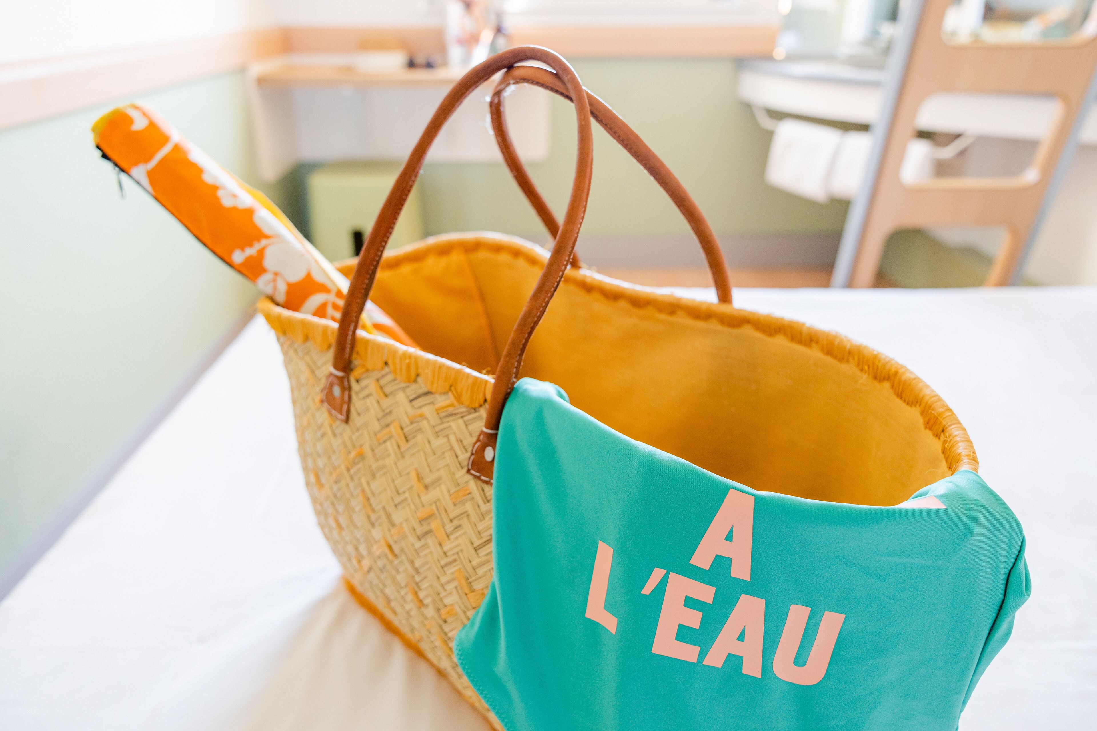A wicker basket with brown handles and a teal bag with "A L'EAU" text.