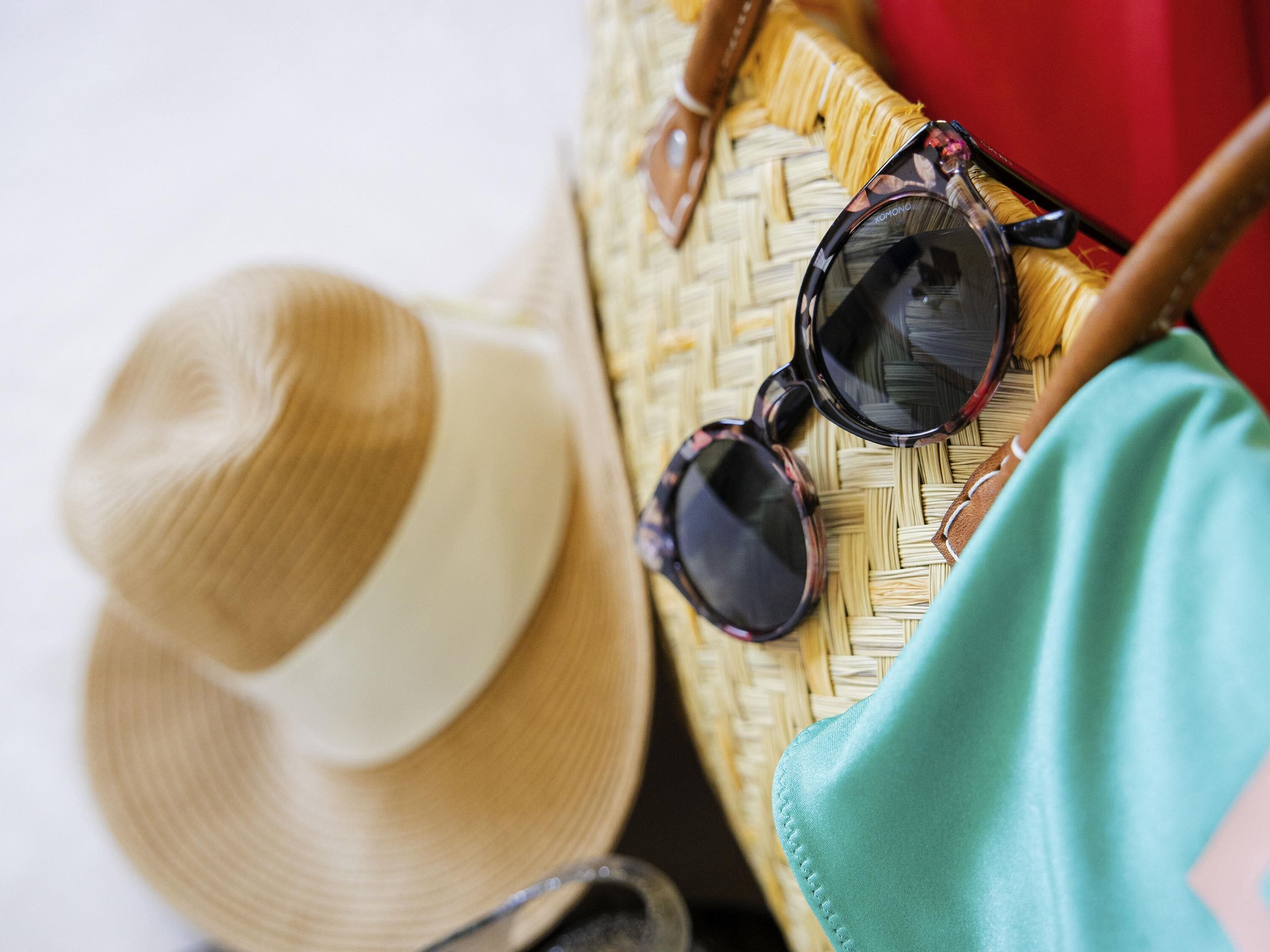 A straw hat, sunglasses, and a woven bag on a surface.